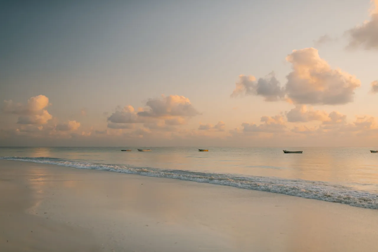 A peaceful tropical beach stretches beneath a soft morning sky, inviting visitors to relax beside the calm ocean.