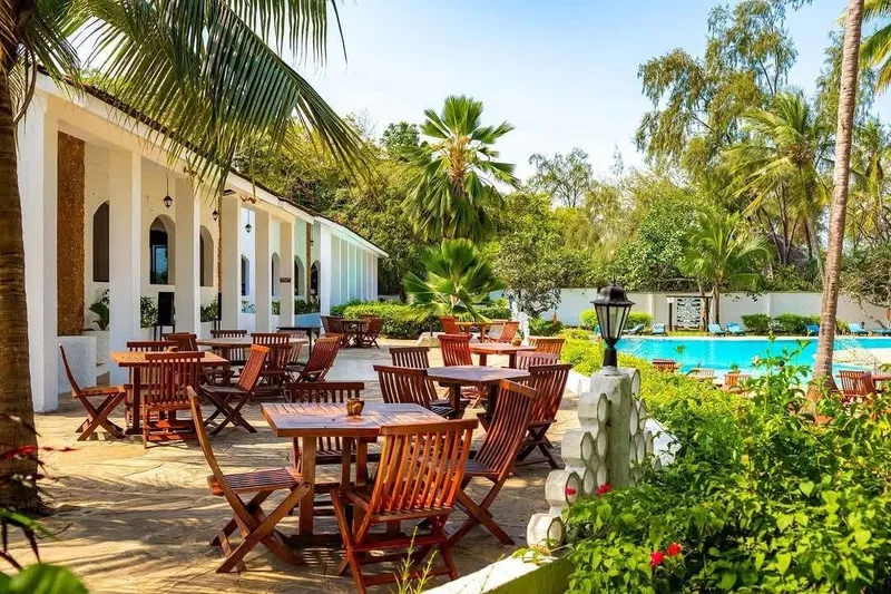 An outdoor patio setup with wooden dining tables surrounded by lush tropical gardens.