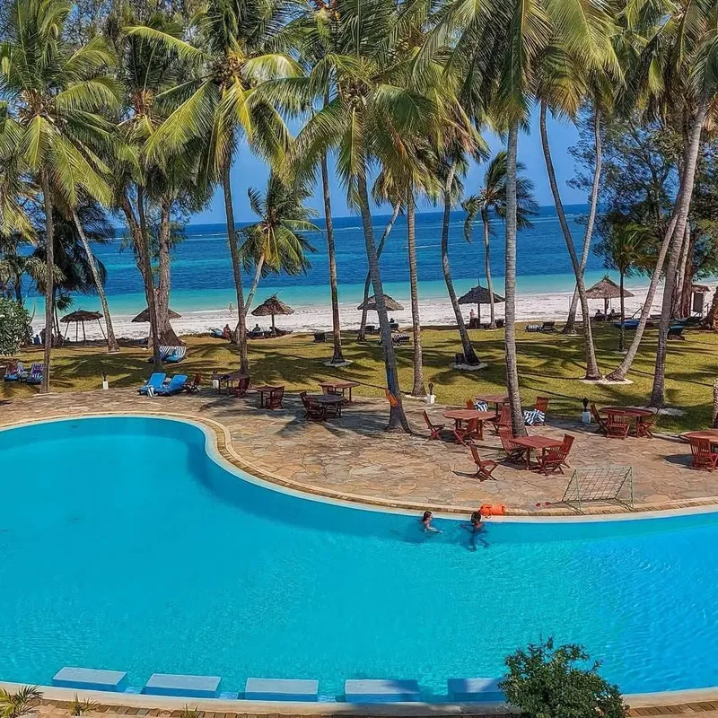 A pristine turquoise swimming pool bordered by swaying palm trees and sparkling waters of the Indian Ocean.